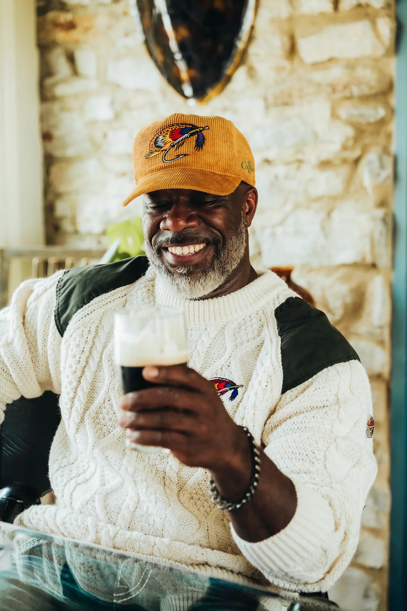 Smiling man in an orange corduroy fly cap and cable-knit sweater